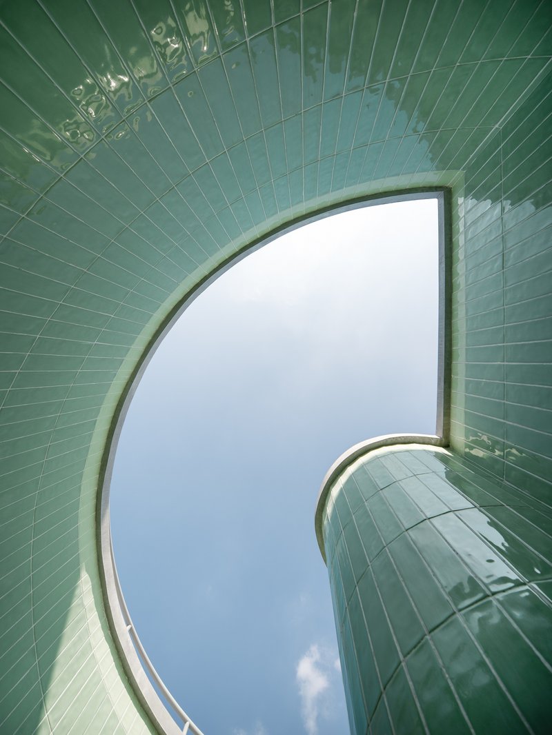 Upward view through curved green-tiled skylight opening framing a patch of overcast sky