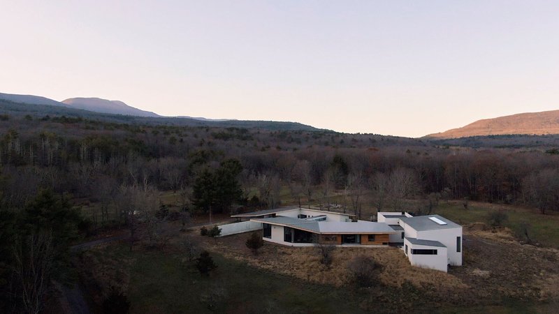 Aerial view of the low-slung residence with metal roofs nestled among bare trees and rolling hills