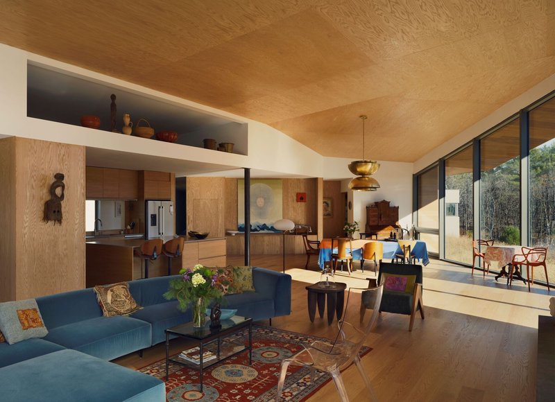 Open living space with vaulted plywood ceiling, oak millwork, and glass doors opening to a courtyard