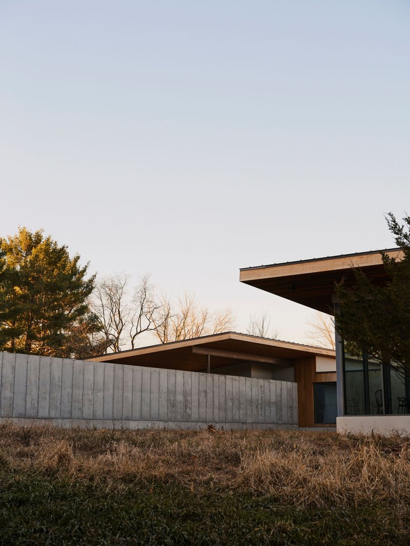 Cantilevered roof overhang above the board-formed concrete wall at dusk with bare trees beyond
