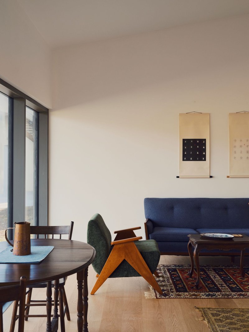 Living area with round dining table, upholstered chairs, floor-to-ceiling windows, and hanging scrolls on the wall