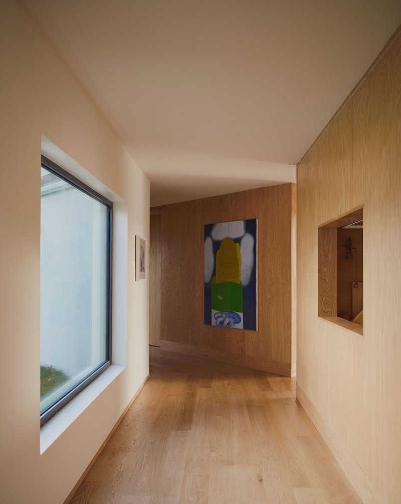 Interior hallway with oak flooring, wood-paneled walls, recessed niche, and framed artwork at the end