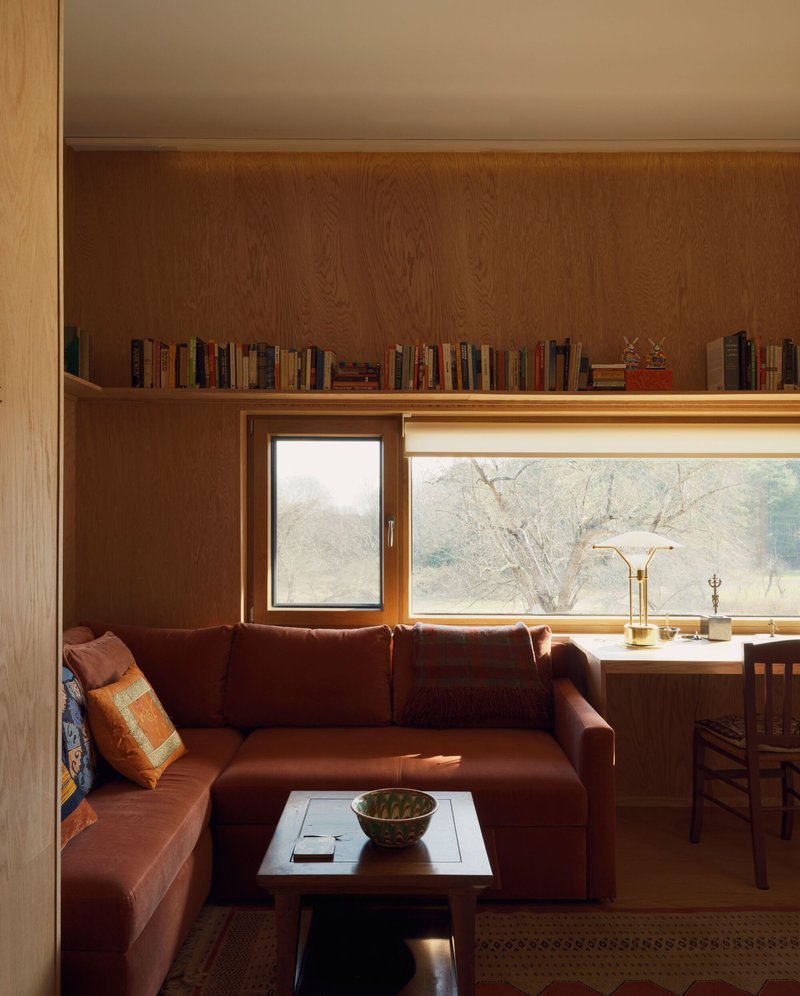 Built-in bookshelf above a corner sofa with horizontal window framing bare trees outside