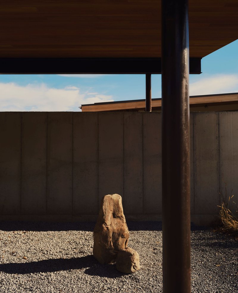 Gravel courtyard with weathered stone sculpture framed by steel column and concrete panel walls