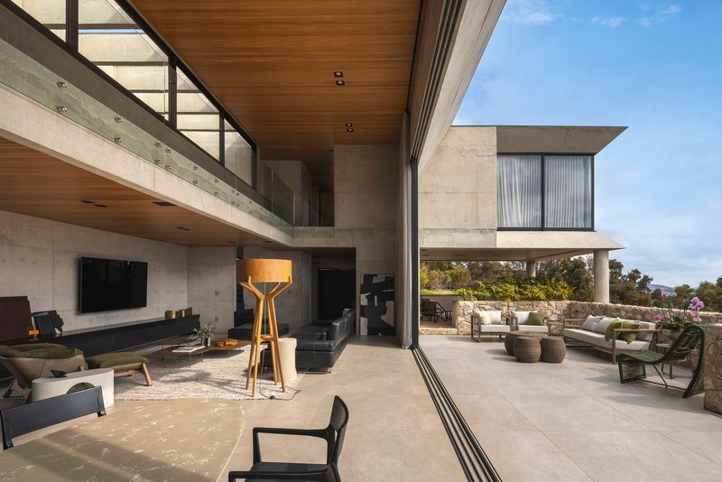 Double height living space opening to a terrace with hillside views under concrete soffits