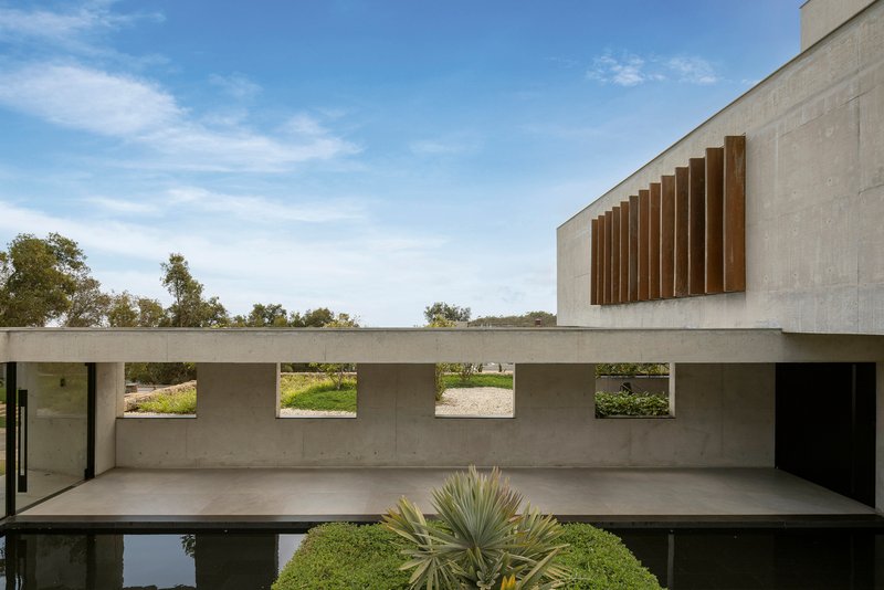 Concrete terrace with horizontal slot windows reflected in a still pool edged by agave plants