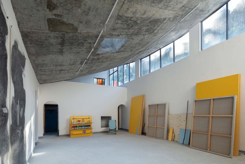 Interior hall with exposed board-formed concrete ceiling and clerestory windows above white walls and stored yellow panels