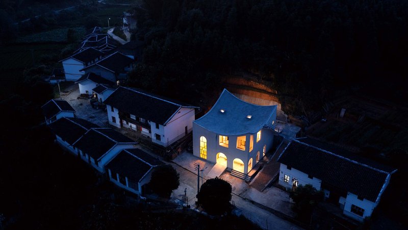 Aerial view at dusk showing the illuminated arched windows against the dark surrounding village rooftops