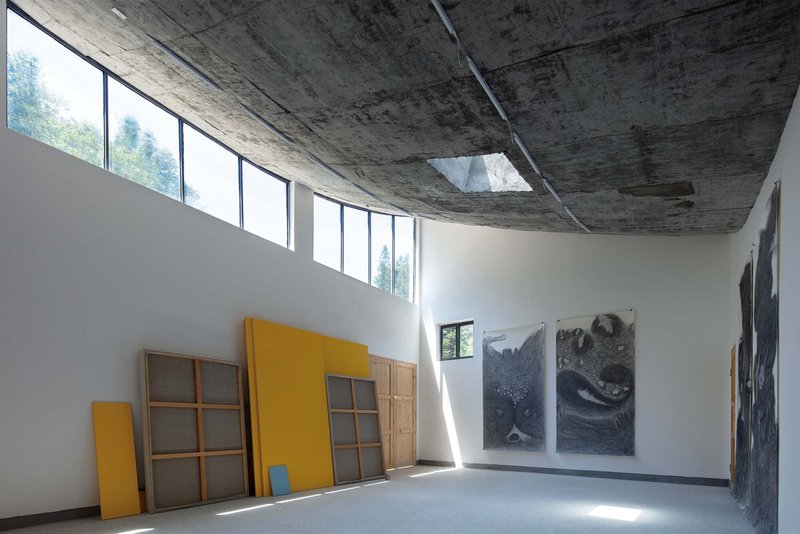 Double-height gallery space with exposed concrete ceiling, clerestory windows, and yellow storage units below