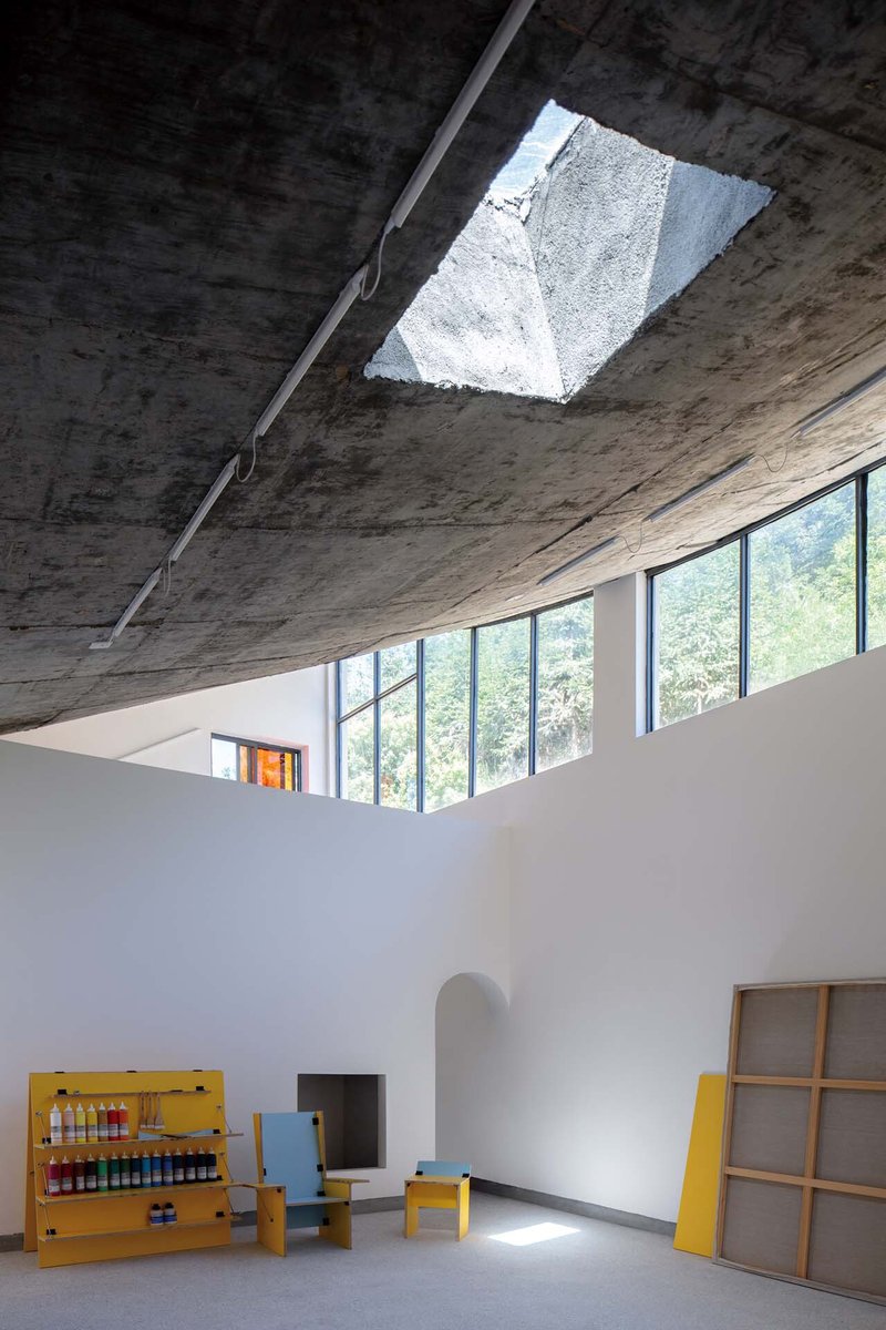 Angular skylight opening in the raw concrete ceiling above white gallery walls with yellow furniture