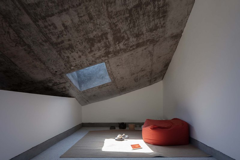 Minimalist room with board-formed concrete ceiling, rectangular skylight, raised platform, and orange bean bag