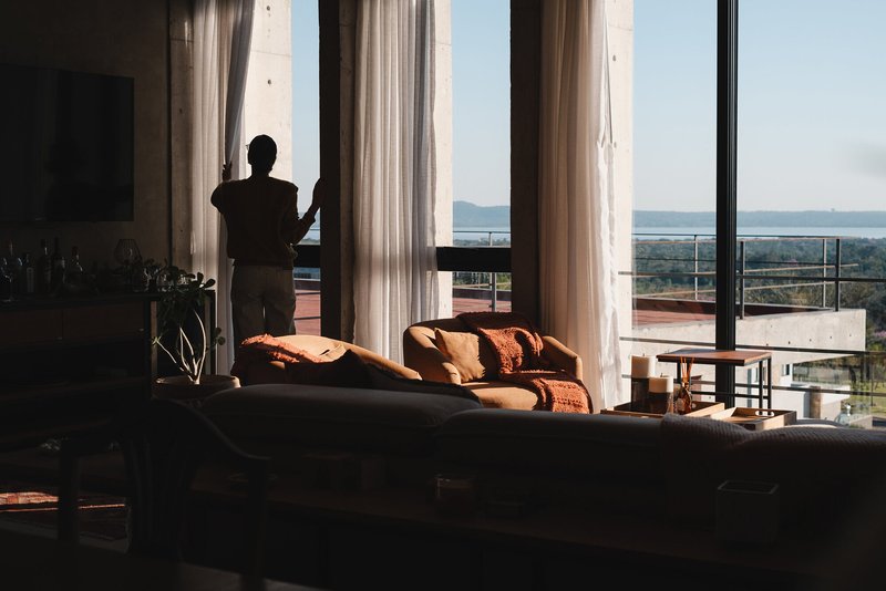 Silhouetted figure at the full-height glazed opening with sheer curtains at dusk