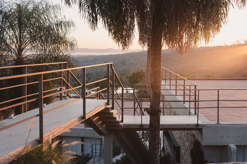 Concrete terrace with metal railings and exterior staircase framed by a palm tree at sunset