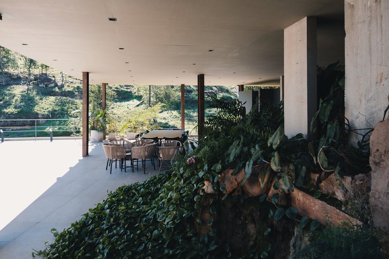 Covered terrace with concrete ceiling, timber columns, dining table, and planted rock garden bed