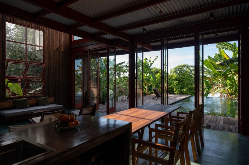 Open living pavilion with folding glass walls framing view of terrace pool and banana trees beyond