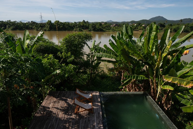 Timber deck terrace with pool and lounge chairs overlooking banana trees and a wide river