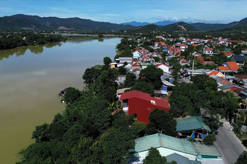 Drone view of the red-roofed residence along a tree-lined riverbank with mountains beyond