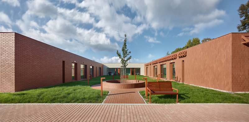 Courtyard with timber decking, circular planter and benches surrounded by red brick and tile walls under clouds