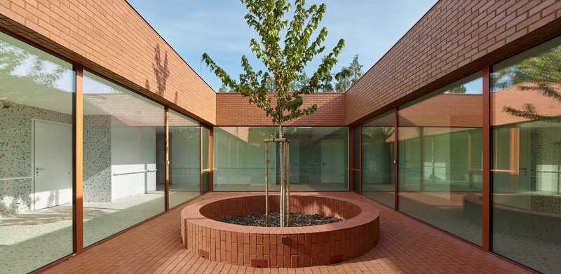 Interior courtyard with circular brick planter bed, young tree and glass walls on three sides