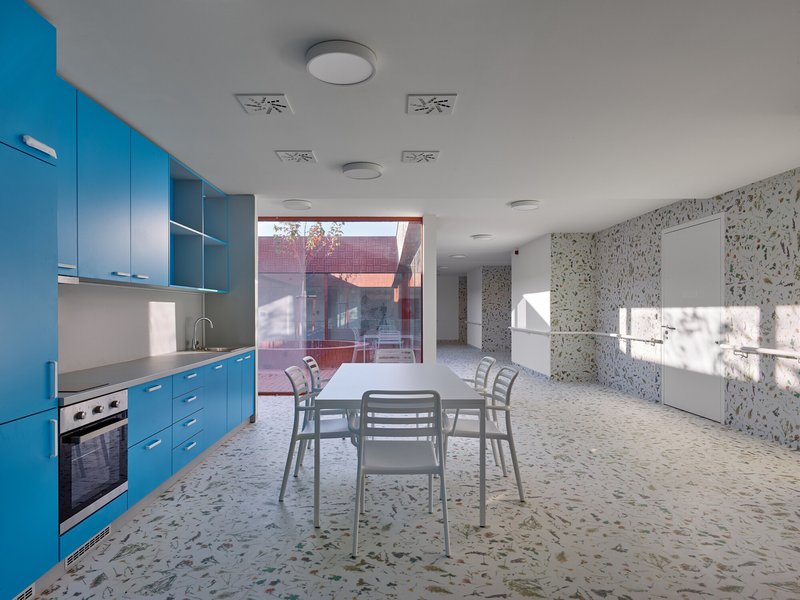 Dining space with blue kitchenette, terrazzo flooring and glass door overlooking the red brick courtyard