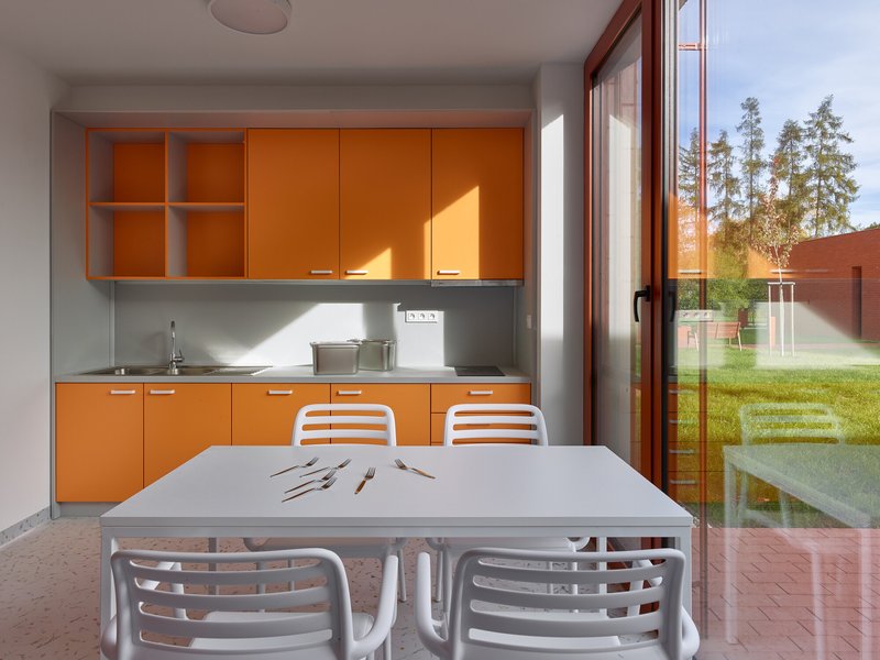 Dining area with orange cabinetry and glass doors opening to a grassy courtyard in afternoon light