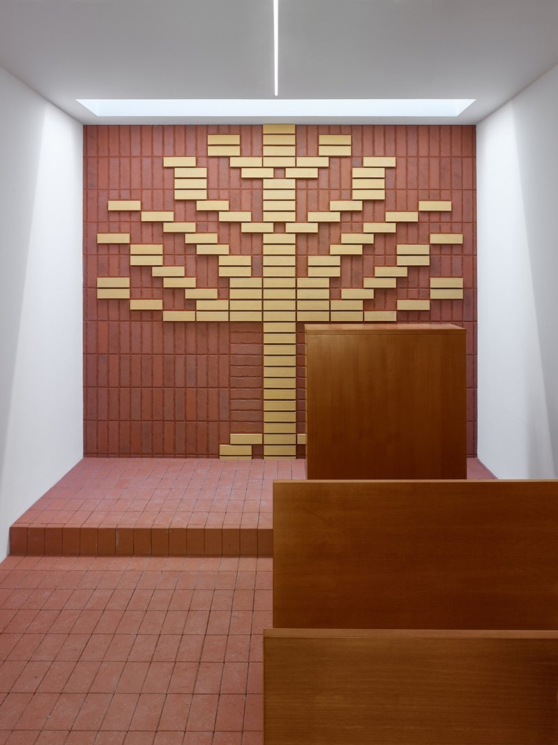 Red tile wall with scattered yellow tile inserts behind timber steps and terracotta floor under a skylight