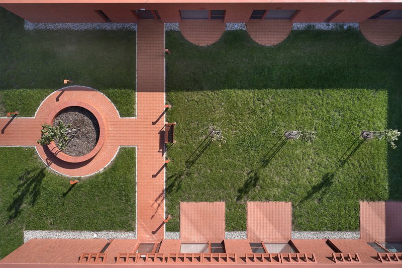 Overhead view of red tile terrace with circular planter, lawn areas, and person walking along the path