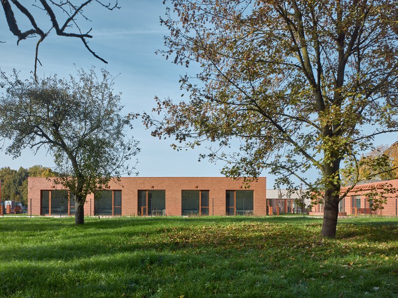 Long facade of red brick tile with large windows framed by autumn trees