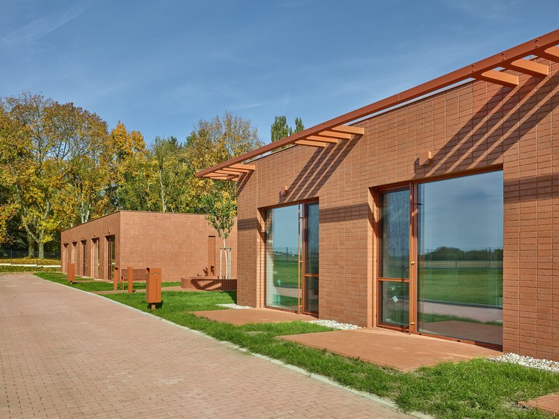 Curved roofline with exposed timber rafters over red brick tile facade and glazed openings