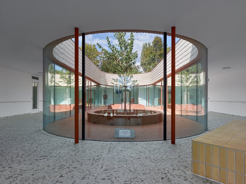 Circular courtyard with curved timber canopy over a central tree and terrazzo floor