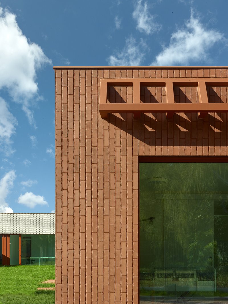 Corner detail of red tile facade with projecting brise-soleil and large green-tinted window under blue sky