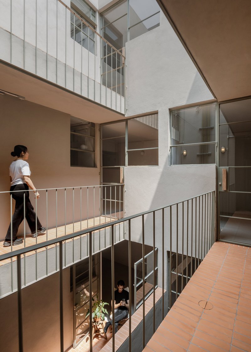 Interior courtyard with metal railings and a person walking on the upper level in daylight
