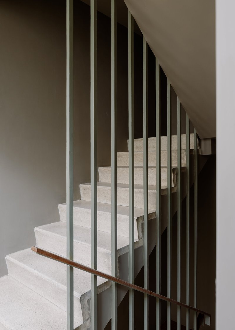 Staircase with vertical metal balusters and a timber handrail ascending between white walls