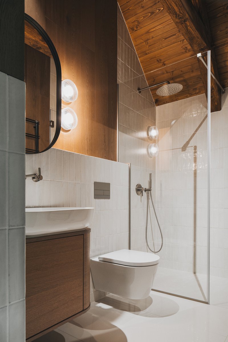 Compact bathroom with glass shower enclosure, timber cabinetry, and an arched mirror above the vanity