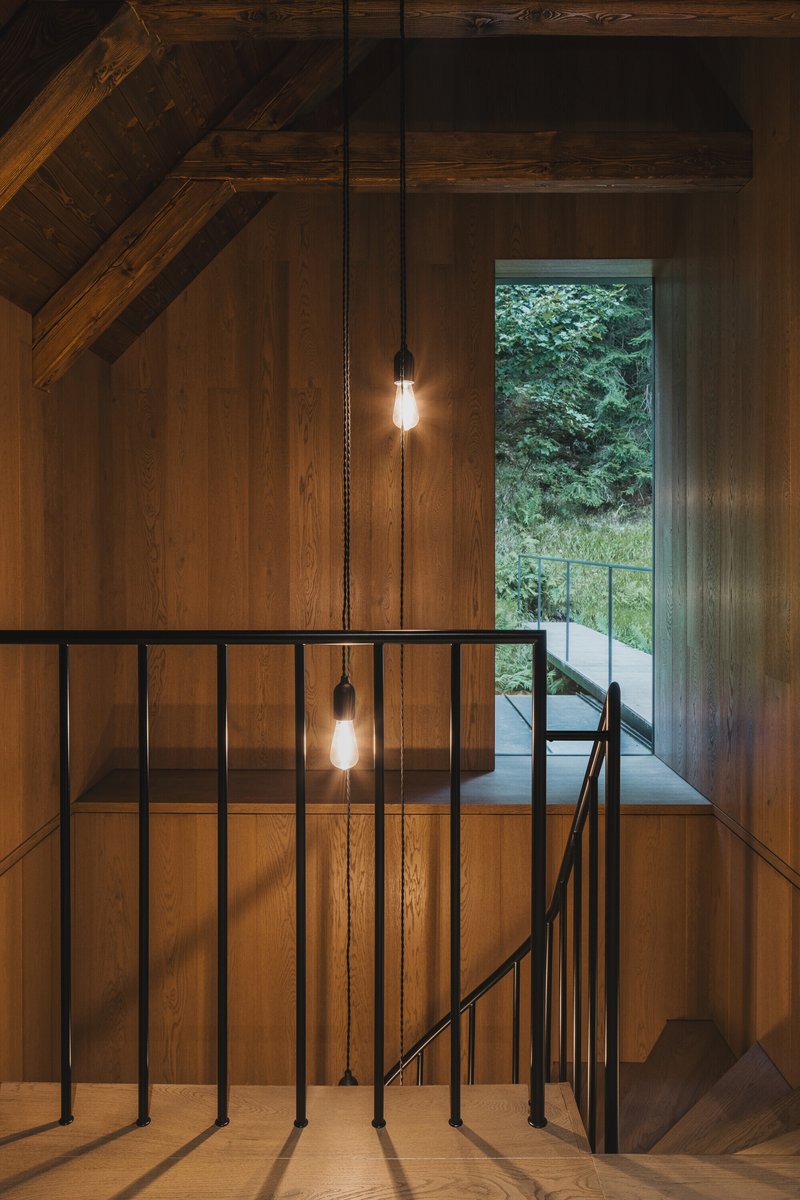Timber-lined stairwell with black metal railing and pendant bulbs illuminated at dusk
