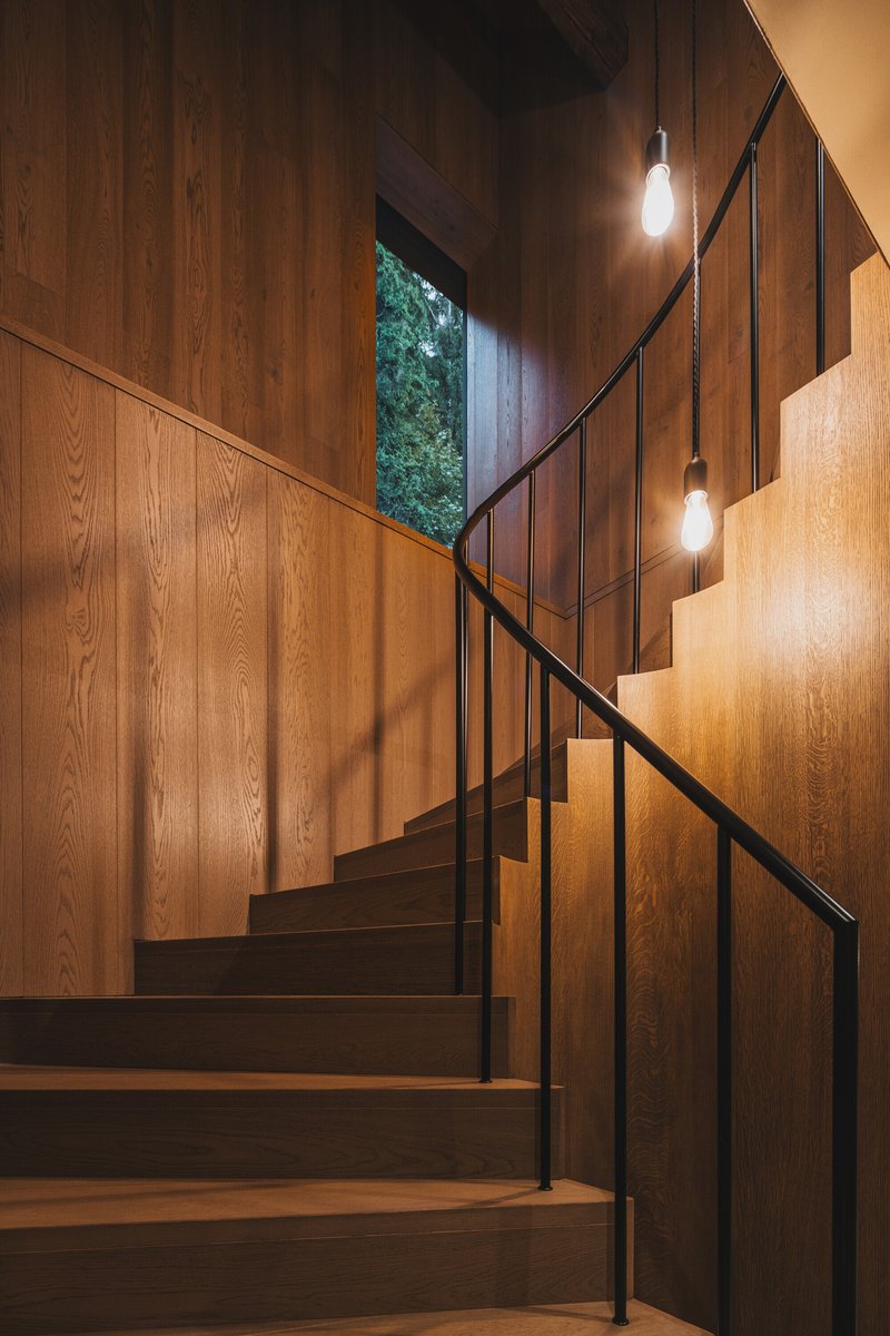 Wooden staircase with black steel handrail ascending past a window opening to greenery