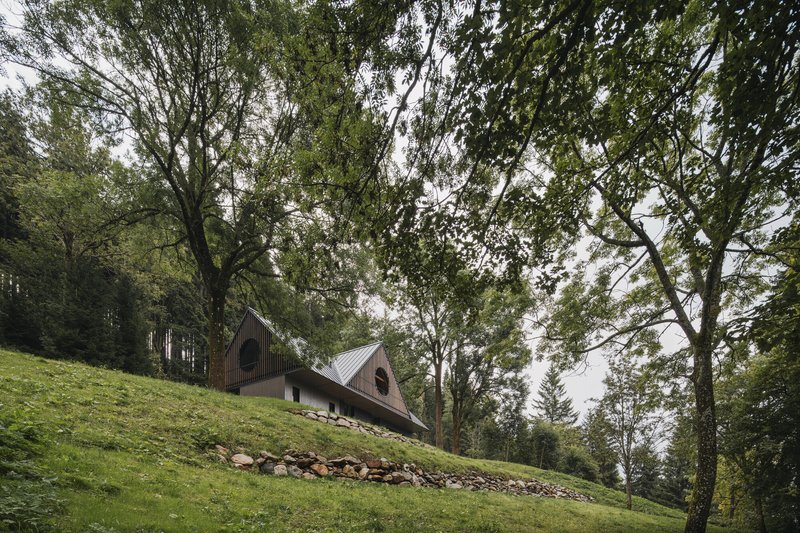 Side view of the dual gable volumes on a grassy hillside with stone retaining wall