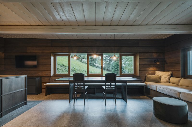 Dining area with timber-paneled walls, built-in benches and pendant lights over a dark table