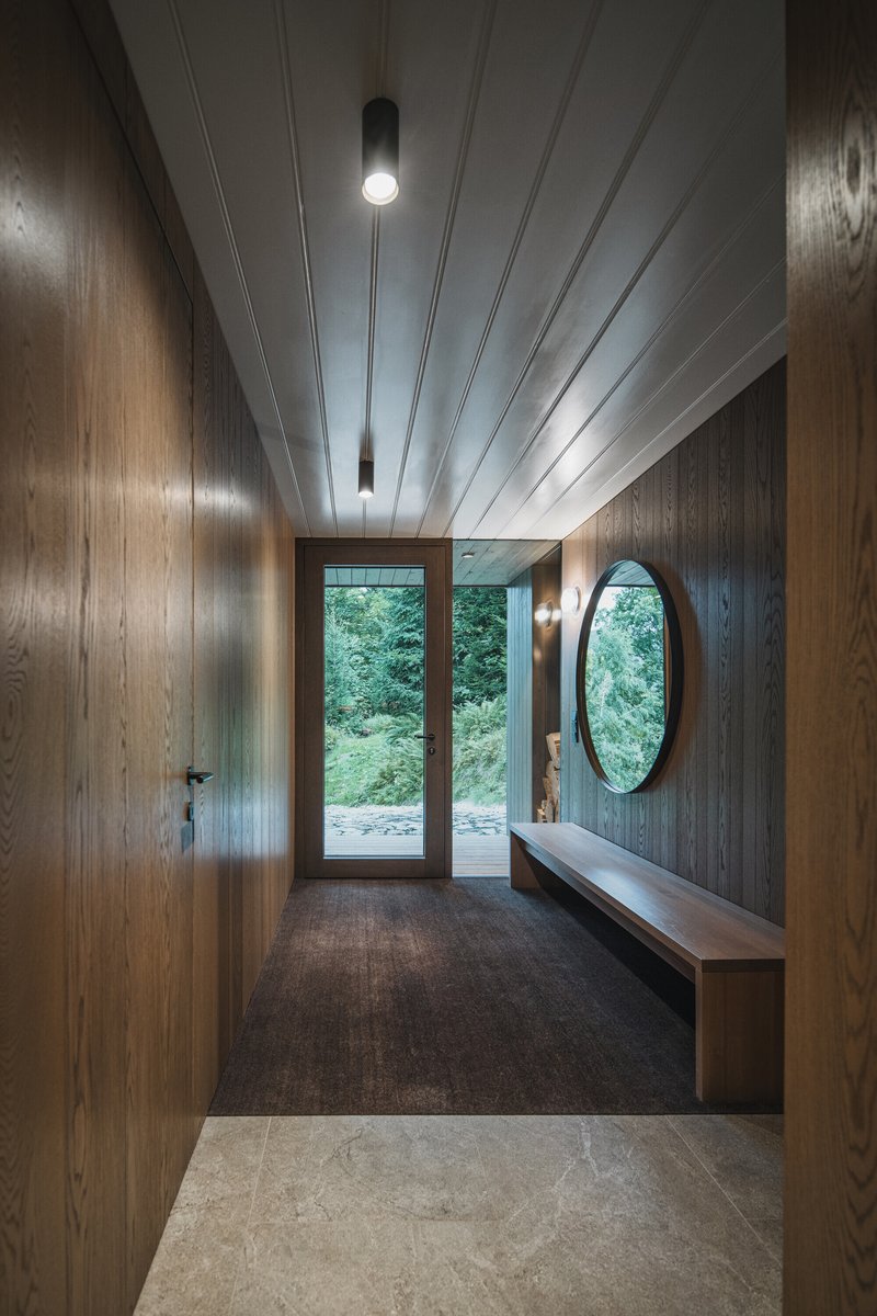 Wood-paneled entry hall with white plank ceiling and glazed door framing greenery beyond