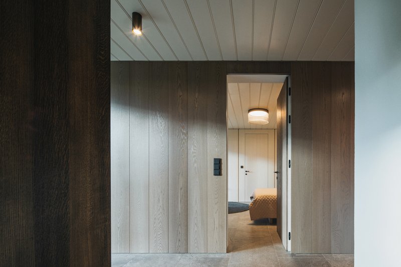 Doorway opening through vertical wood-clad walls revealing a corridor with ceiling-mounted fixtures
