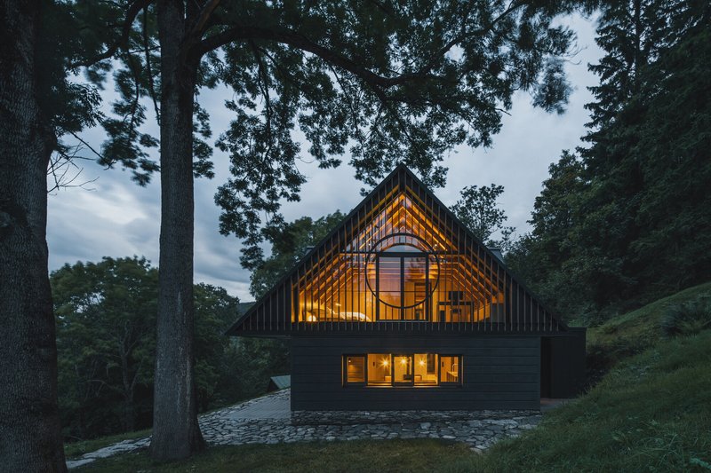 Dark vertical timber facade with arched upper window and standing seam metal roof at dusk