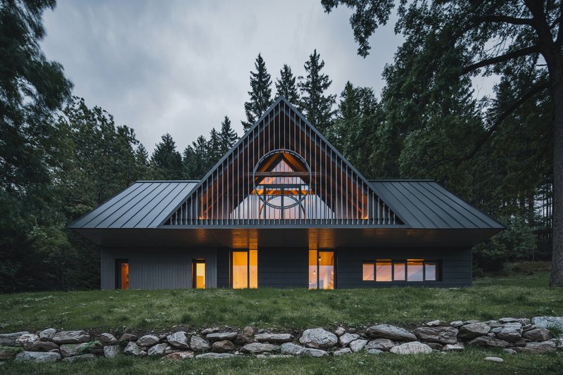 Front elevation showing symmetrical gable with arched window and stone retaining wall in evening light