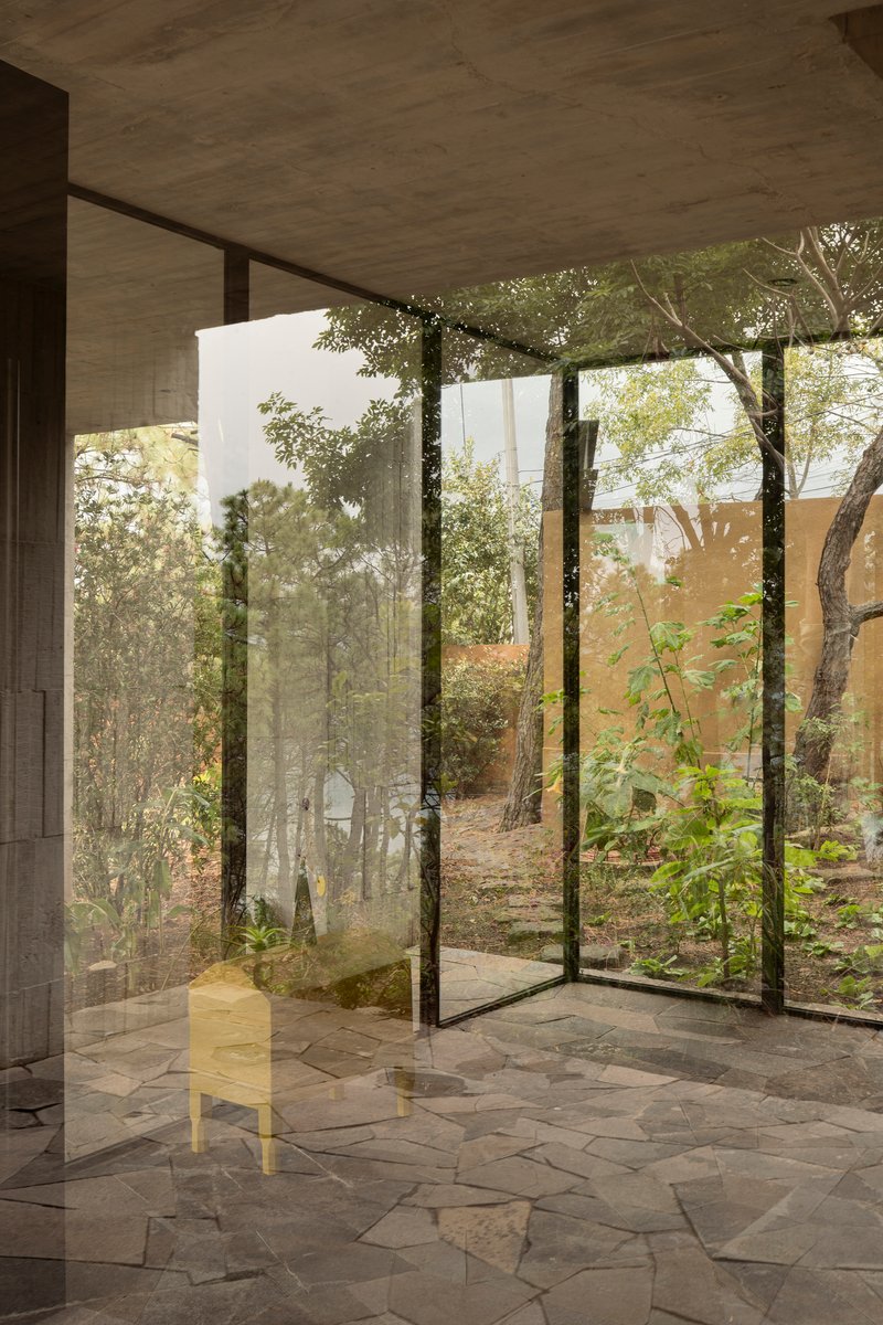 Floor-to-ceiling glass corner opening onto a planted courtyard with existing trees and stone paving