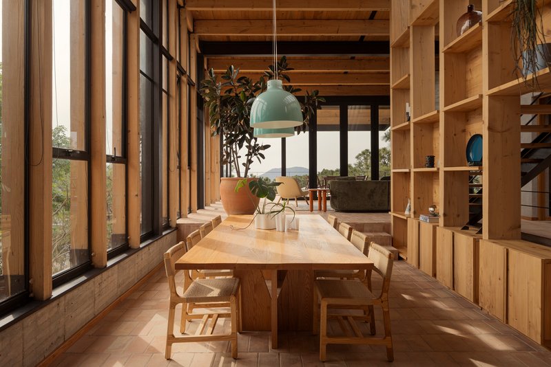 Dining area with exposed timber ceiling beams and floor-to-ceiling plywood shelving under soft afternoon light
