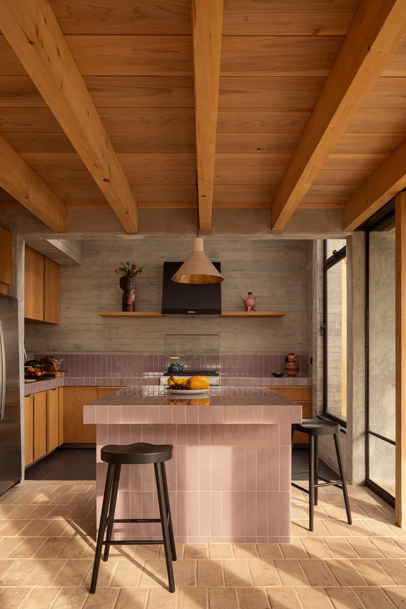 Kitchen with pink tiled island and board-formed concrete backsplash under an exposed timber joist ceiling