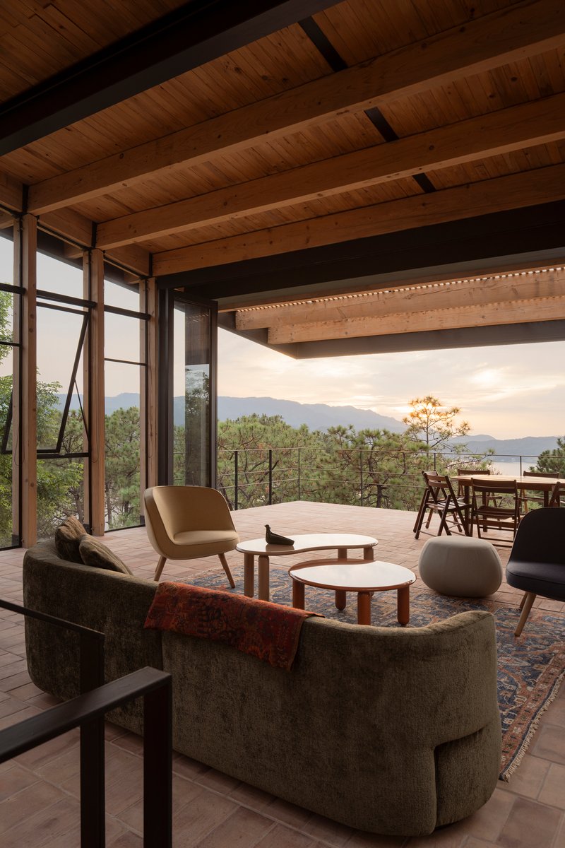 Living room with curved sofa looking through steel-framed windows toward distant mountains at dusk