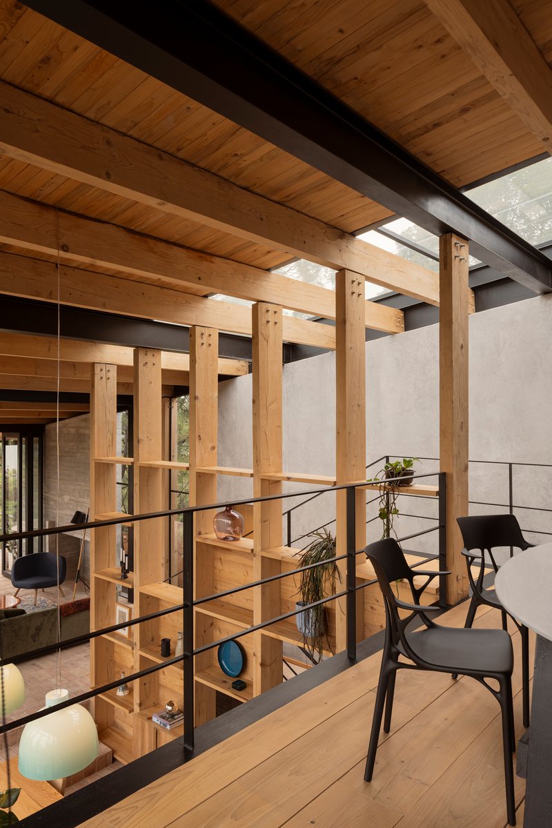 Timber shelving screen with metal railing dividing upper level beneath wood plank ceiling and black steel beams