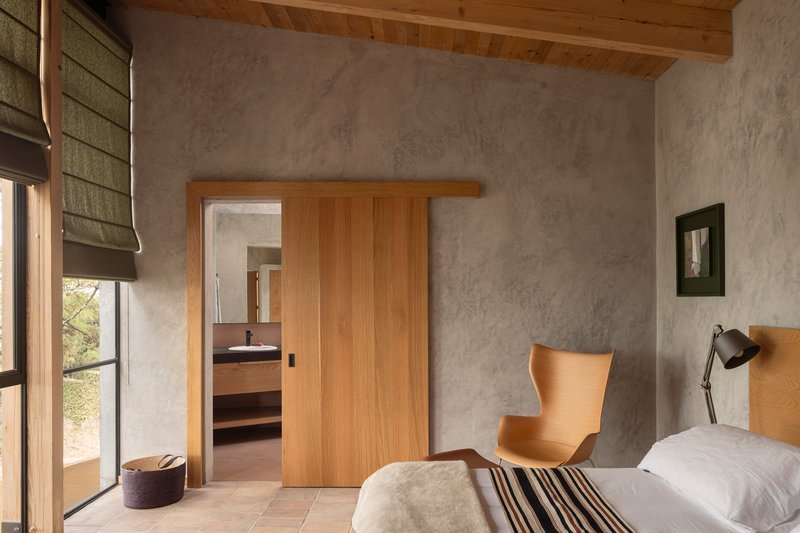 Bedroom with sliding timber doors opening to an ensuite beneath an exposed wood beam ceiling