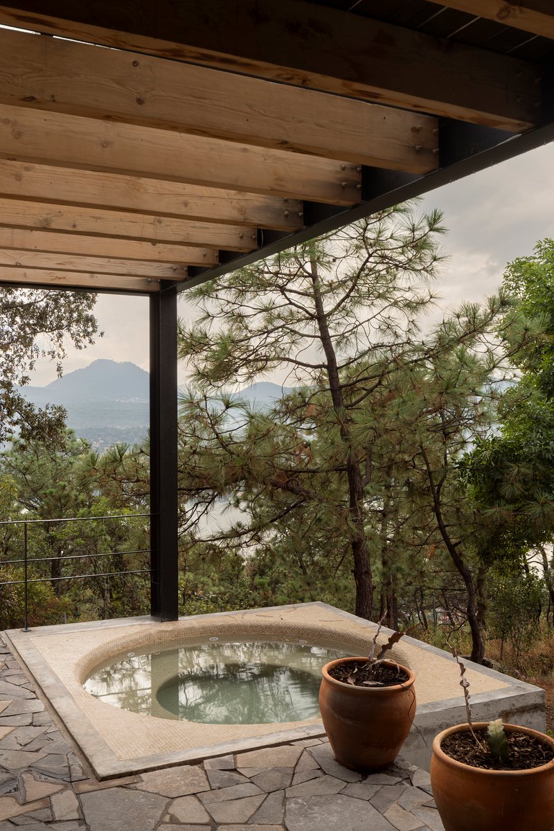 Sunken stone-clad plunge pool on a terrace framed by timber beams and cable railing overlooking forested hills