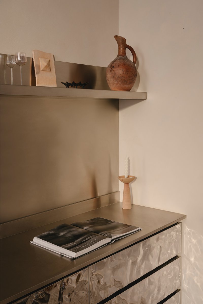 Detail of metallic cabinet with textured surface below a shelf holding a terracotta vessel